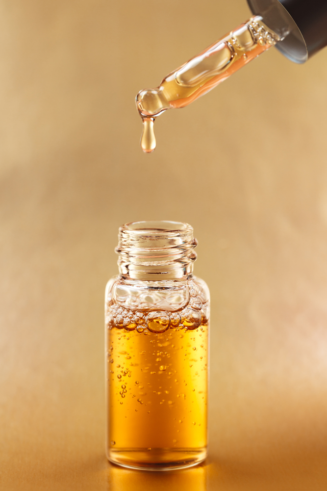 Bottle of cosmetic oil with pipette on golden background. Front view.